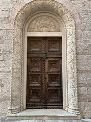 Old wooden oak door with a carved pattern and a stucco bas-relief on top of a stone wall