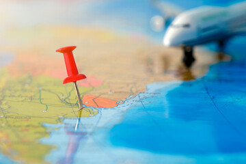 a close-up of a pushpin stuck in a map, with an airplane in the background. The concept is travel,...