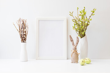 Home interior with easter decor. Mockup with a white frame and willow branches in a vase on a light...
