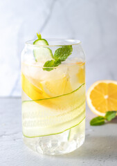lemonade with cucumber slices, ice, lemon and mint in a glass on a light background. Refreshing summer drink made of fruits and vegetables