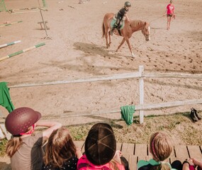 Nauka jazdy konnej  na padoku . Dzieci obserwują lekcje jazdy konnej swojej koleżanki z obozu konnego