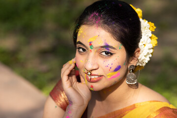 Holi festival of color, young beautiful girl woman lady in indian attire saree with dry organic color or colour or gulal or abeer or Holi powder on her face