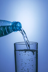 Pure water pours from a plastic bottle into a glass on a blue background