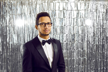 Portrait of young African American man in formal suit and glasses on glitter disco background....