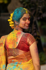 Young beautiful girl or woman or lady in indian attire saree looking back with dry organic color or colour or gulal or abeer or Holi powder on her face, Festival of color holi - obrazy, fototapety, plakaty