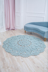 In a bright room on the floor there is a round blue handmade carpet. flooring, natural cotton. Blue knitted handmade carpet on the floor