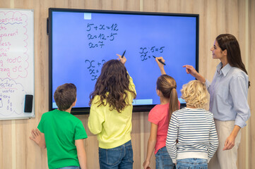 Back view of children and teacher standing near blackboard