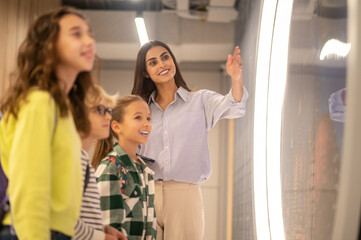 Obraz premium Teacher pointing to side and smiling children watching
