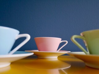 Row of vintage pastel tea cups on yellow table against petrol background. Afternoon tea party.