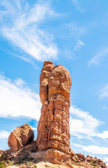 Lone hoodoo spire sandstone outcropping stands on hill beside fallen rock against blue sky in Arches National Park Utah USA.