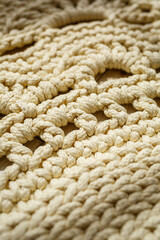 Homemade knitted carpet made of thick threads, made by hand: a handmade rug made of beige threads lies on the floor, the sun shines on it