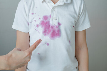 Female finger points to a dirty stain spilled juice on a white children's t-shirt. The concept of cleaning stains on clothes. 