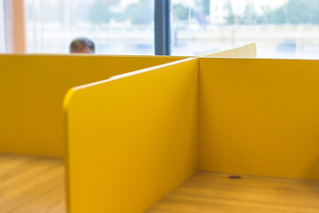 View of modern office space interior with desks in yellow tones with workers, employee with a laptop on a cozy workplace in the background, it-company open space with tables, chairs and rooms