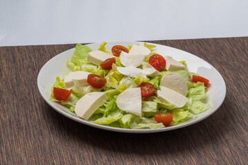 Healthy food. Green lettuce, small tomatoes, natural white cheese on a white plate.