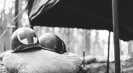 Metal Helmets Of United States Army Infantry Soldier At World War II. Helmets Near Camping Tent In Forest Camp. black and white photography
