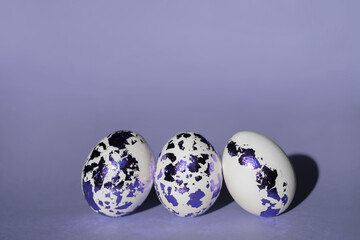 Three Easter white eggs decorated with colored blue-purple foil on a Very Peri color background. Fashionable stylish painted eggs. 