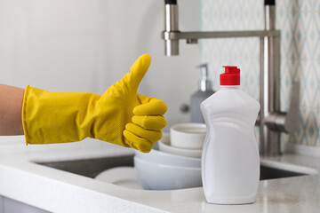 A white bottle with dishwashing gel and a hand in a yellow rubber glove waggles its thumb up on a...
