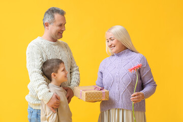 Little boy and his grandparents with presents on yellow background