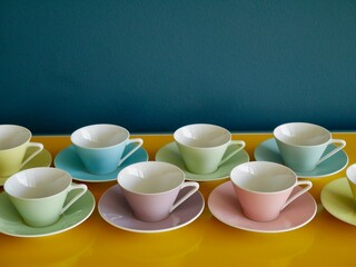 Row of vintage pastel coffee cups on yellow table against petrol background. Afternoon coffee party.