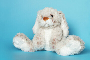 Stuffed bunny on blue background. Easter concept. Cute white toy bunny sitting on colored background.