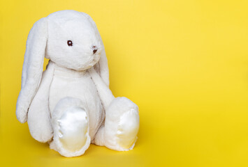 Stuffed bunny on yellow background. Easter concept. Cute white toy bunny sitting on colored background.