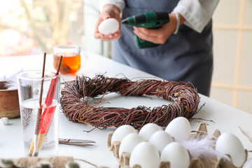 Woman decorating Easter wreath with egg on white table