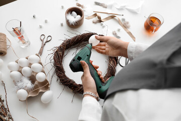 Woman decorating Easter wreath with egg on white table