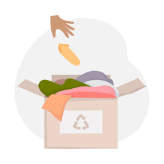 Cardboard box with old clothes for recycling. Black hand throws the sock into the box