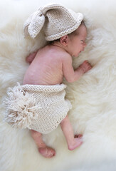 Baby in a bunny costume sleeping on a white sheep fur. High quality photo
