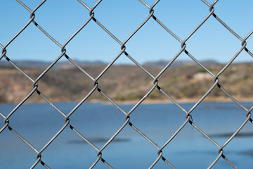 Close-up Of Chainlink Fence Against Lake and a hill