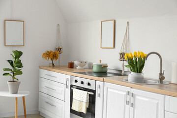 Tulips in sink and utensils on kitchen counters near white wall