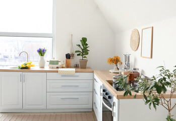 Kitchen counters with beautiful flowers and utensils near white wall