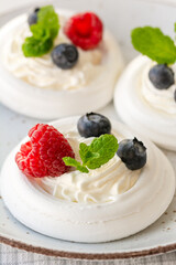 Meringue nests with whipped cream, raspberries, blueberries and a mint leaf