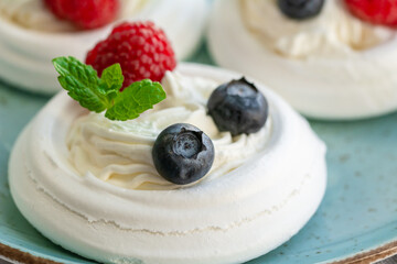 Meringue nests with whipped cream, raspberries, blueberries and a mint leaf