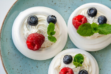 Meringue nests with whipped cream, raspberries, blueberries and a mint leaf