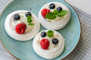 Meringue nests with whipped cream, raspberries, blueberries and a mint leaf