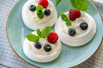 Meringue nests with whipped cream, raspberries, blueberries and a mint leaf