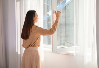 Pretty young woman opening window in room