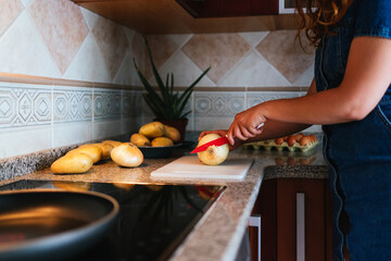 A young Caucasian housewife cutting onions with a knife on the cutting board in the kitchen