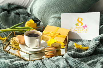 Tray with tasty breakfast, gift, greeting card and flowers for International Women's Day celebration on bed