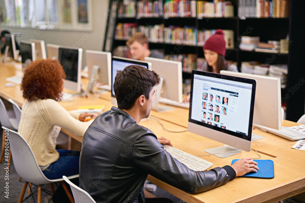 Poster Gathering information for his research project. Shot of students working on computers in a university library.