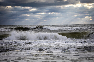 crashing waves at beach with cloudy sky and rays of light through clouds in background