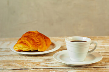 Coffee in a white ceramic mug. Croissant with coffee for breakfast. Coffee on an old wooden table.