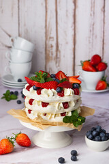 Multi-layered Pavlova dessert with fresh strawberries, blueberries, and whipped cream on a rustic wooden background.