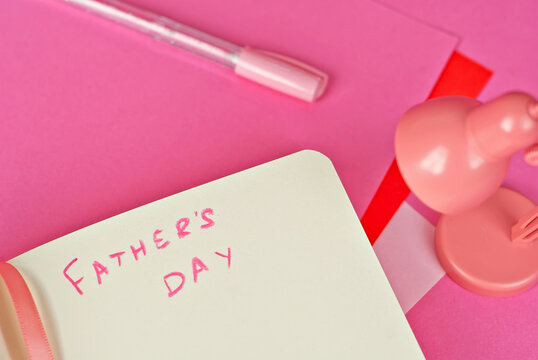 Notebook on a pink background. Toy table lamp near the notebook. Copy space and free space for text in notebook. Mockup for design. The word "father's day" is written in pencil. Creativity concept.