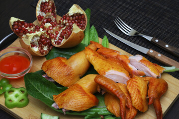 Pieces of smoked chicken on lettuce leaves with vegetables and pomegranate on a serving board