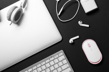 Modern laptop, keyboard, earphones and PC mouse on dark background, closeup