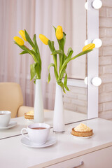 Client's place in hairdressing and beauty salon with cup of tea, cake and yellow tulips in vase. Spring decor.