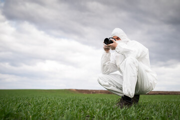 Young scientist and geologist taking pictures of the land to inspect and take to the lab. Biologist wearing a protective suit and a face mask. 