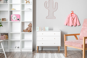 Interior of light children's room with big shelving unit and chest of drawers